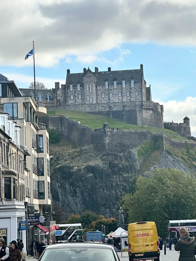 El castillo de Edimburgo sobre su peñasco, encima de una calle concurrida y la bandera de Escocia