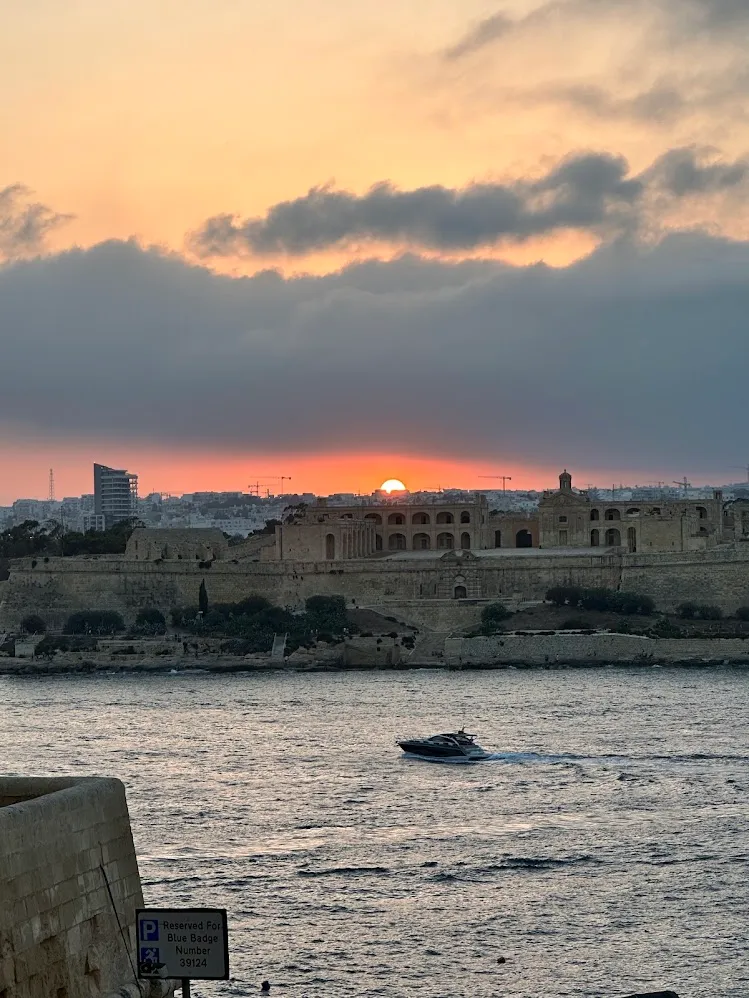 Un barco cruzando el puerto frente a las fortificaciones de Malta al atardecer