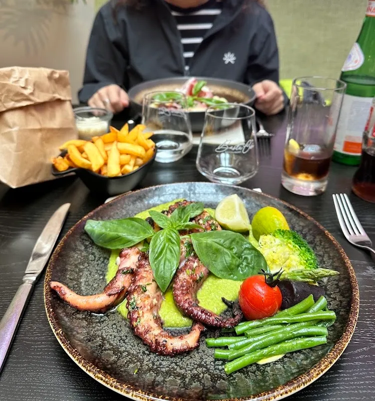 Un plato de pulpo a la parrilla con verduras y papas fritas en una mesa de restaurante