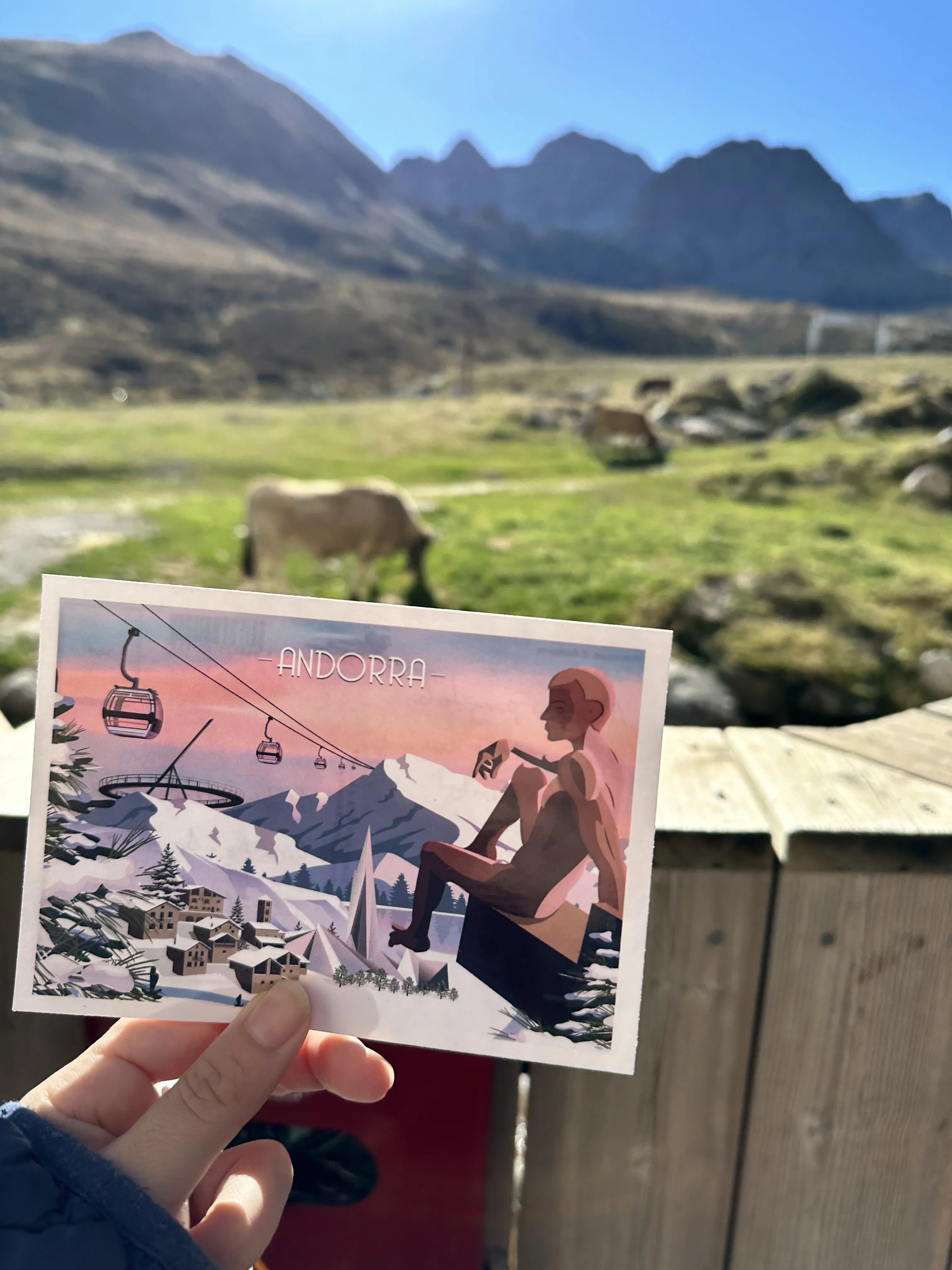 Una postal de Andorra frente a vacas pastando y las cumbres de los Pirineos