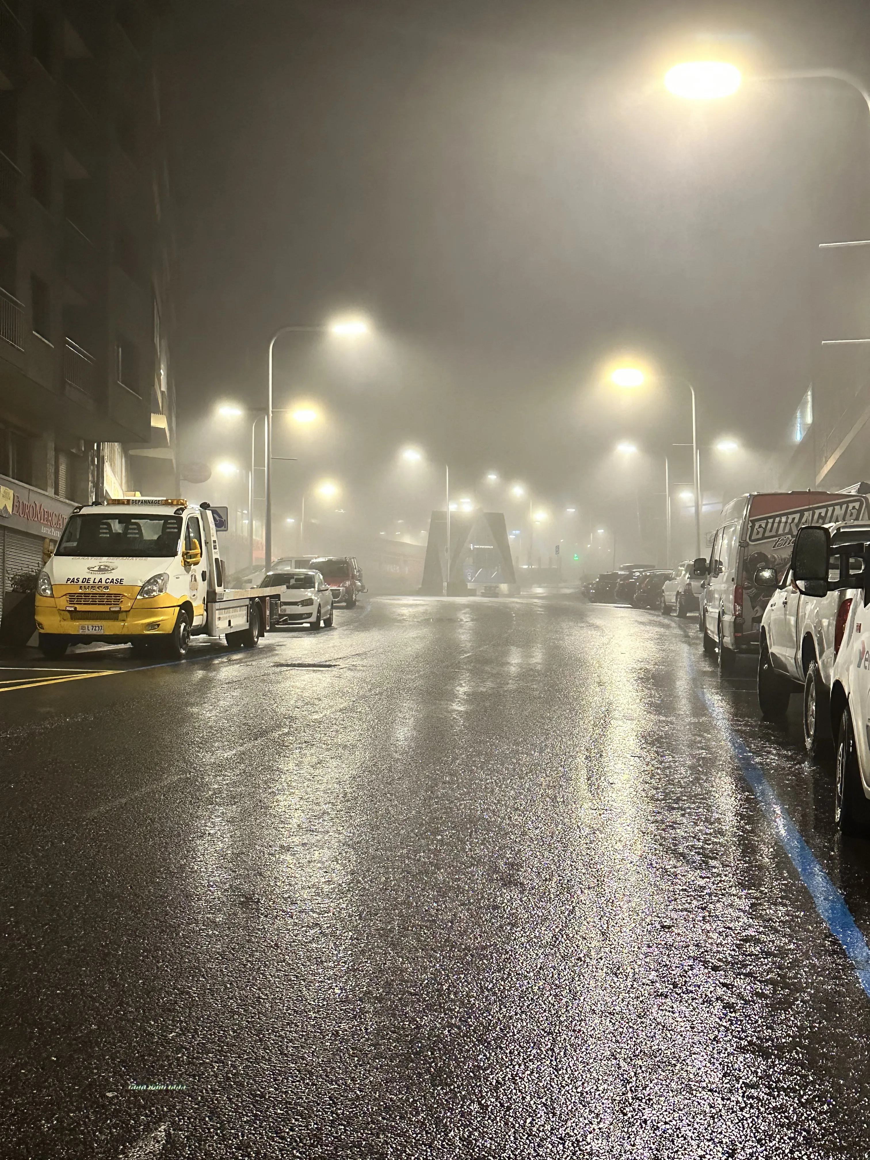 Una calle mojada por la lluvia iluminada bajo la niebla en Pas de la Casa