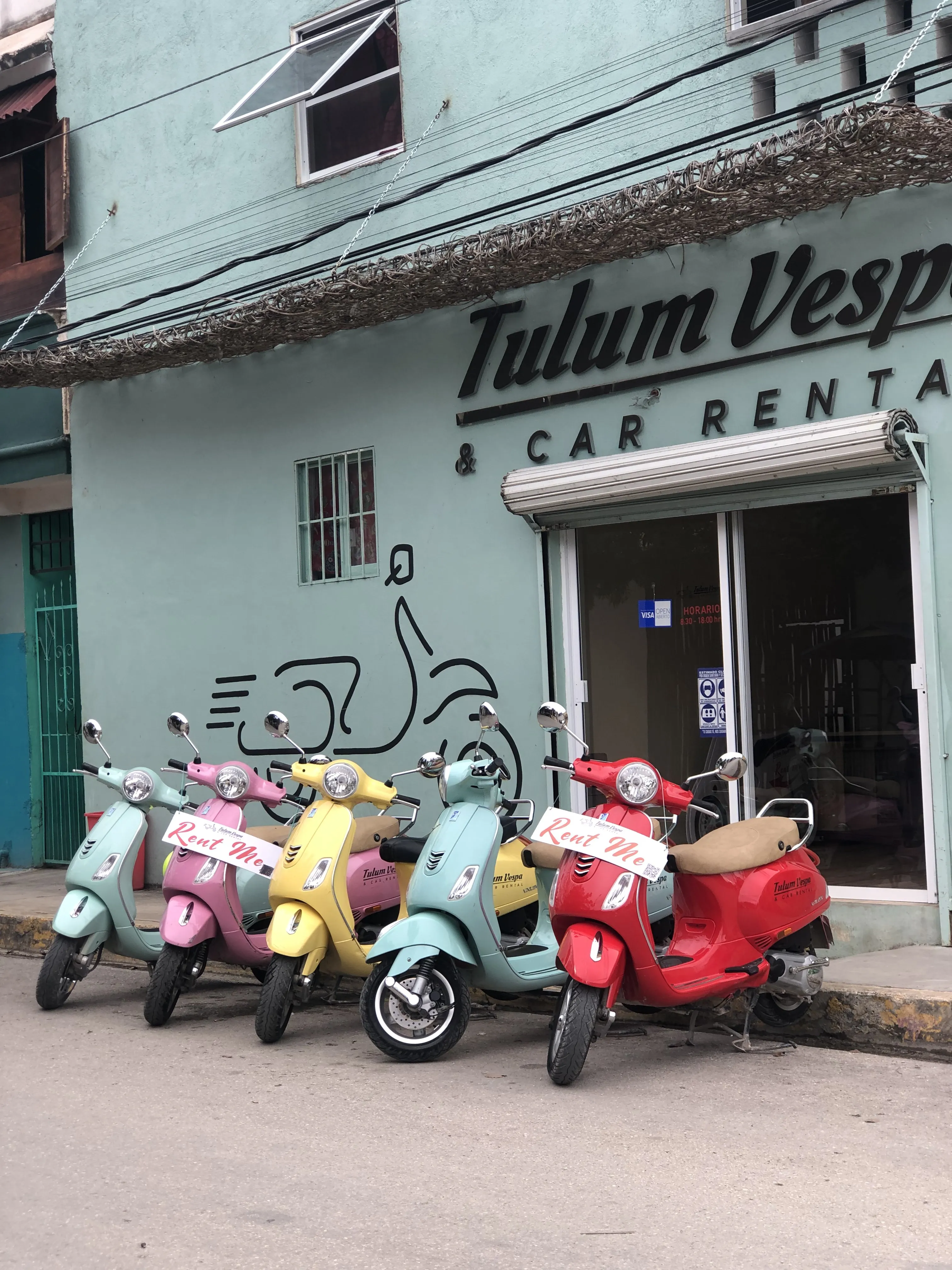 Scooters de alquiler de colores alineados frente a un local en Tulum