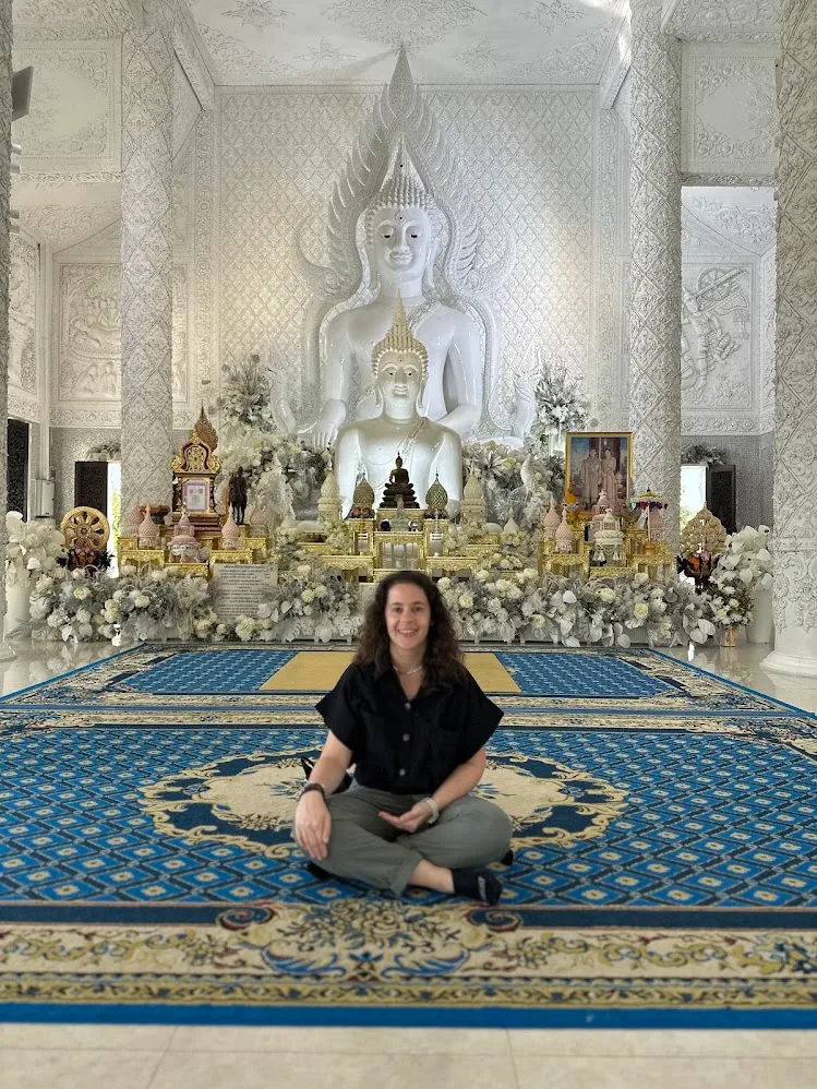 Una viajera sentada frente a estatuas blancas de Buda dentro de un templo